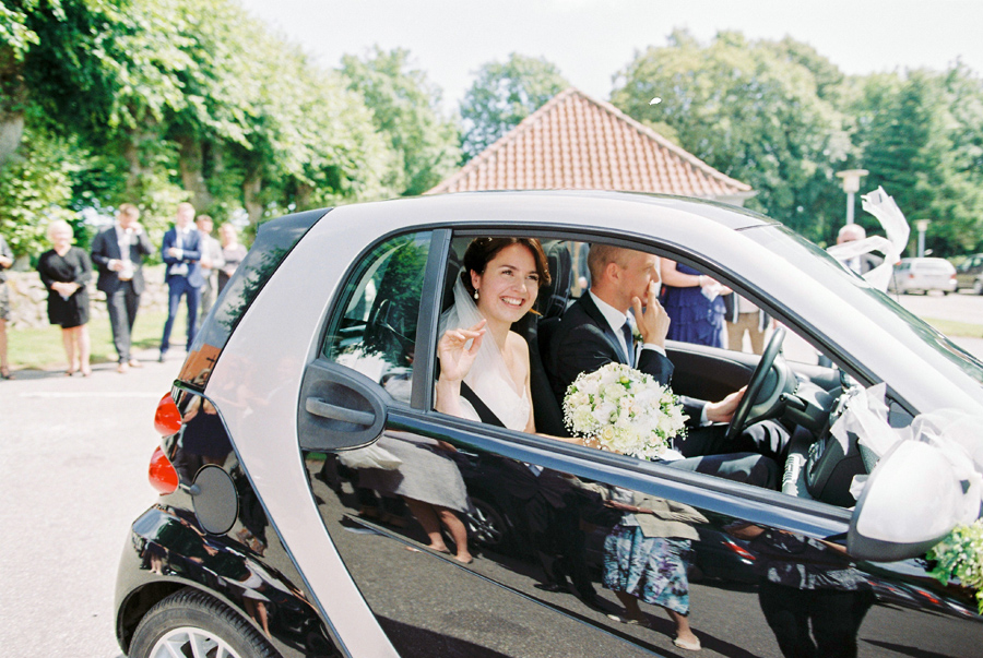 bride and groom drive off in Smart Car