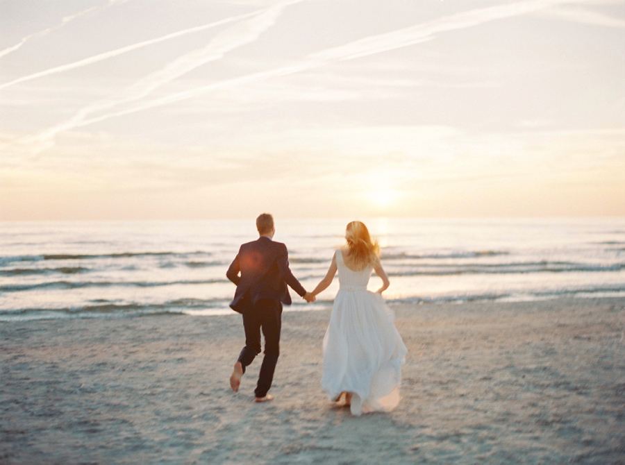 Bride and groom running hand in hand on the beach at sunset