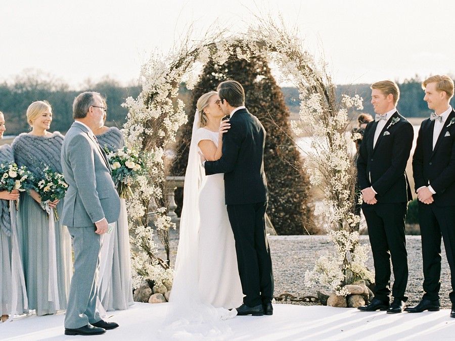 bride and groom share a kiss under their winter white wedding arbor