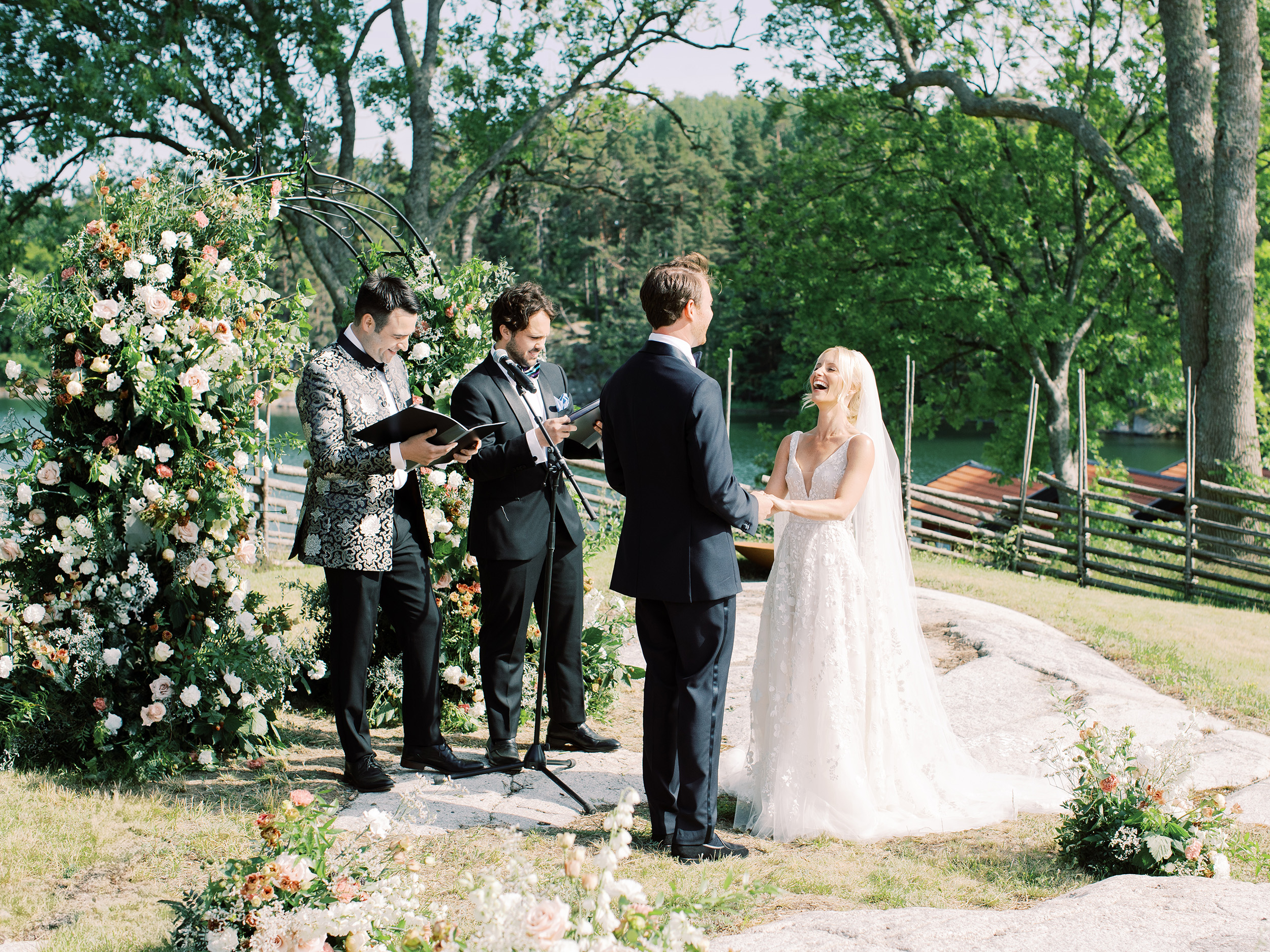 A luxury wedding the the archipelago in Sweden where the bride and groom laugh and say I do in front of a large floral arch.