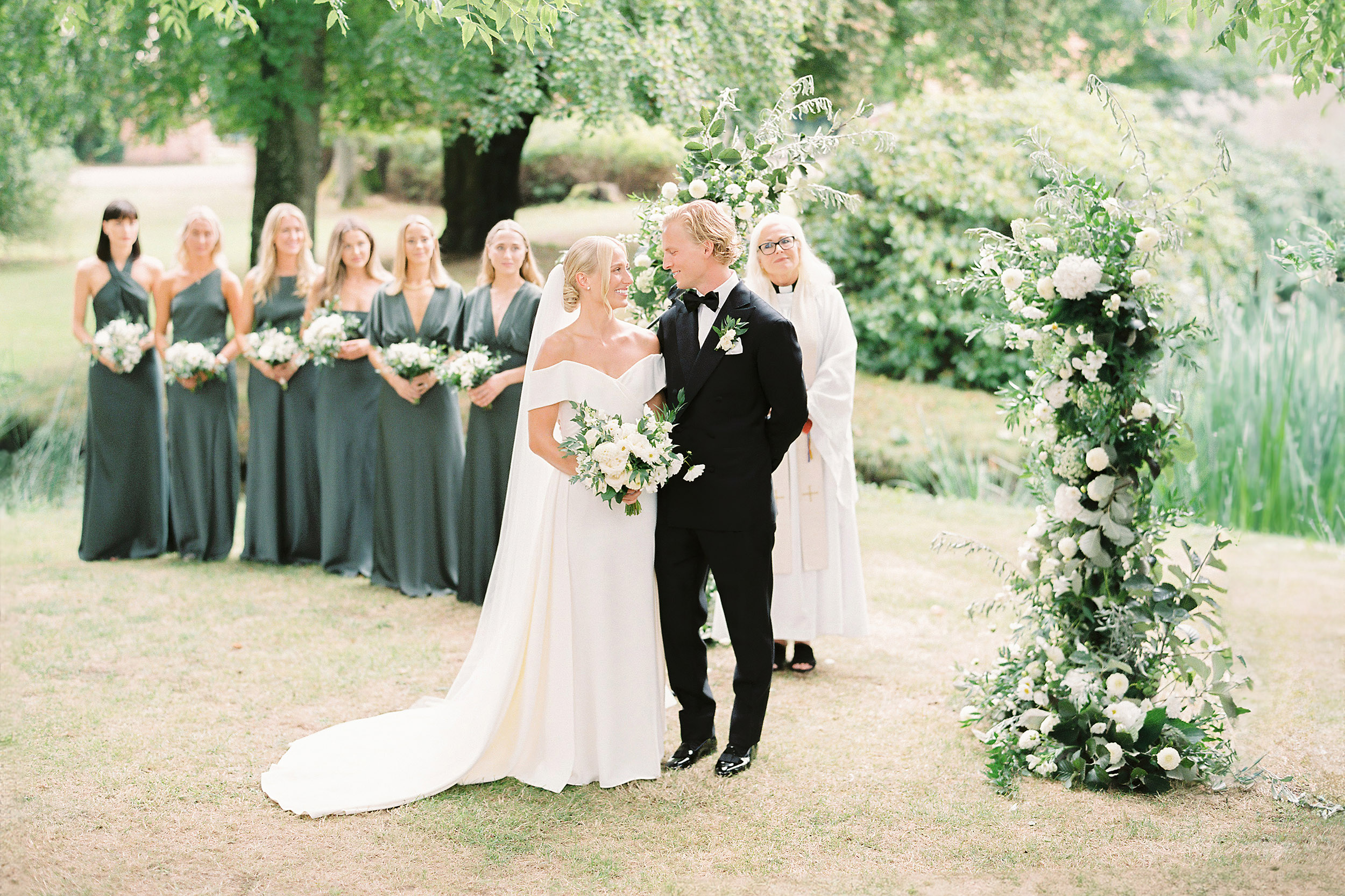The bride and groom standing in front of a large floral arch in the garden at Jordberga Skåne.