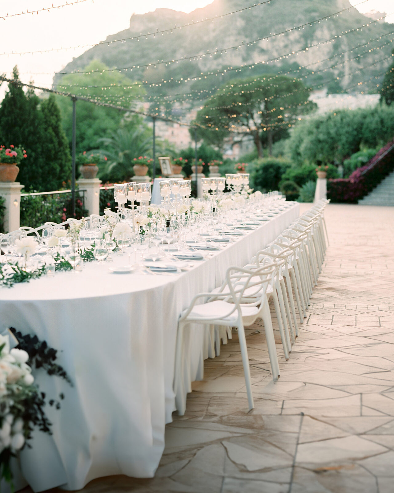 An elegantly set outdoor dining table with white chairs under twinkly lights, at the Grand Hotel Timeo Terazzo in Sicily.