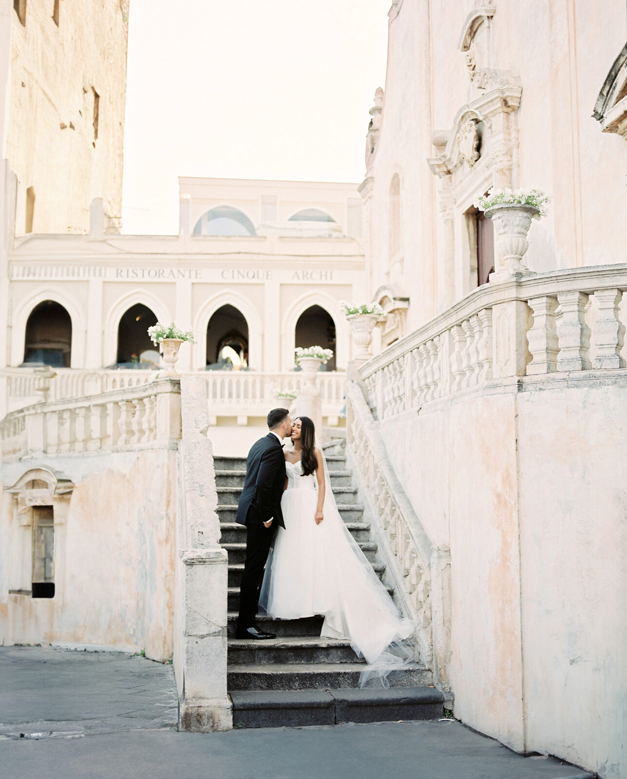 Bride and groom sharing a kiss on a historic staircase at the piazza in Taormina, Sicily.